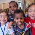 Four young students smile for a photo in a classroom.